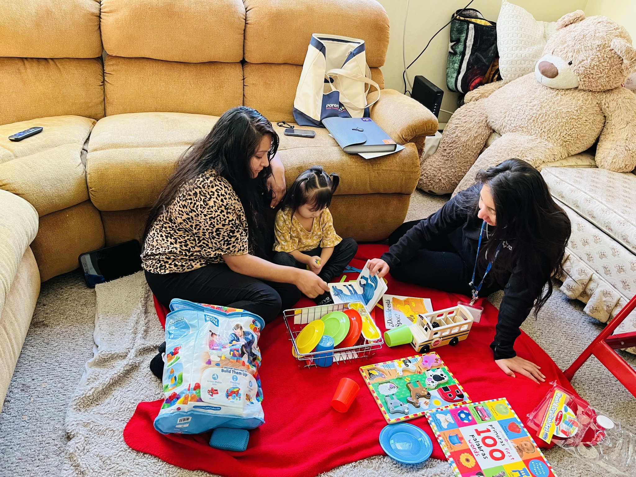 two women sit on floor with toddler while playing with toys